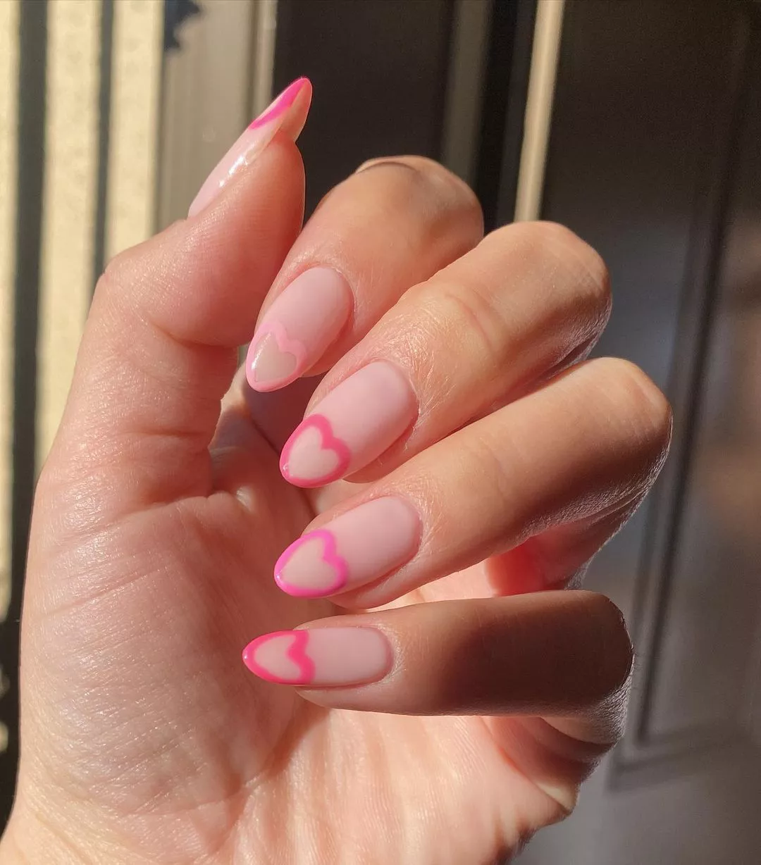 Person with medium-length, almond-shaped nails, which have negative space pink hearts on the tips