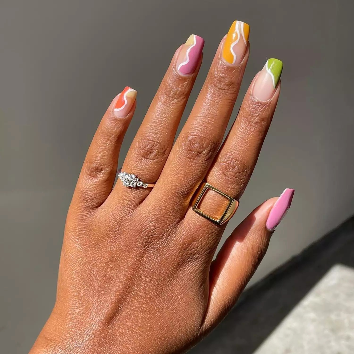 Person shows their colorful nails with white swirl borders on each finger