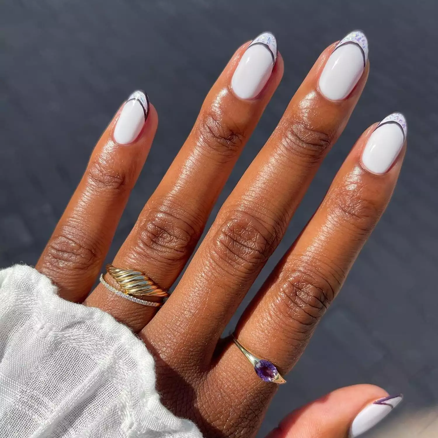 Person showing off their white manicure, outlined with a dark purple polish and glitter French tips