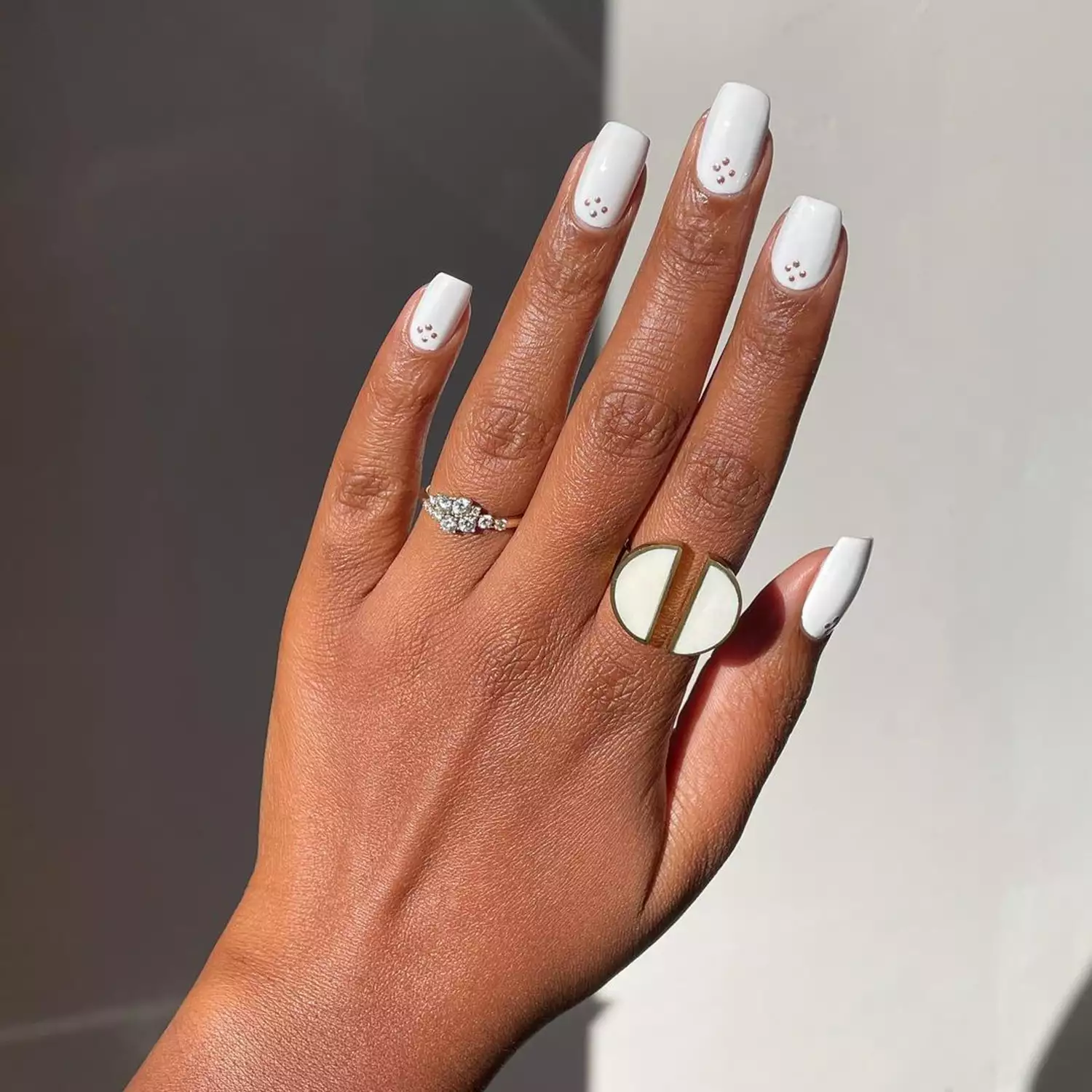 Person showing off their simple white manicure, which is square-shaped and has gold dots at the base