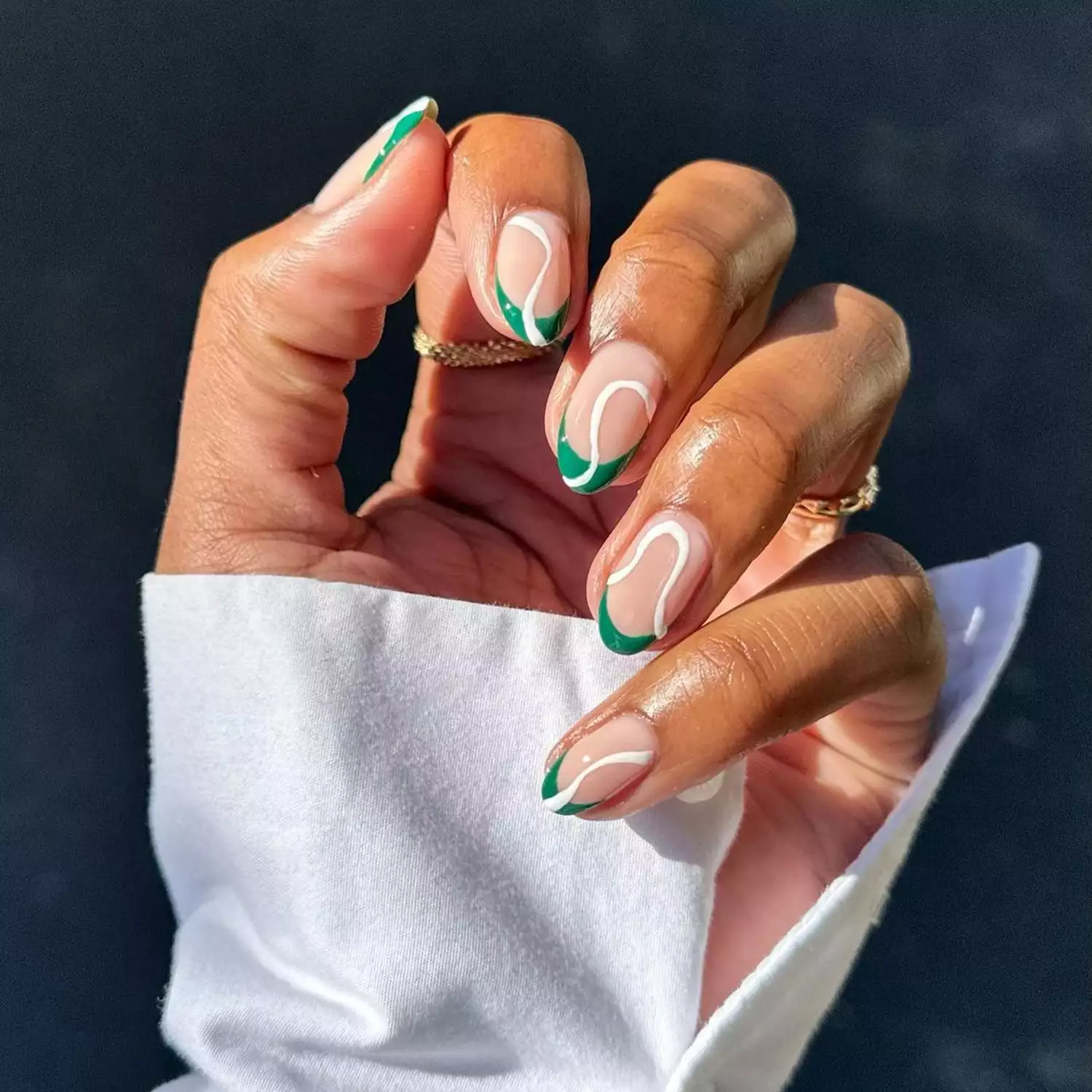 Person shows off their manicure, which features thin, green French tips and white swirls