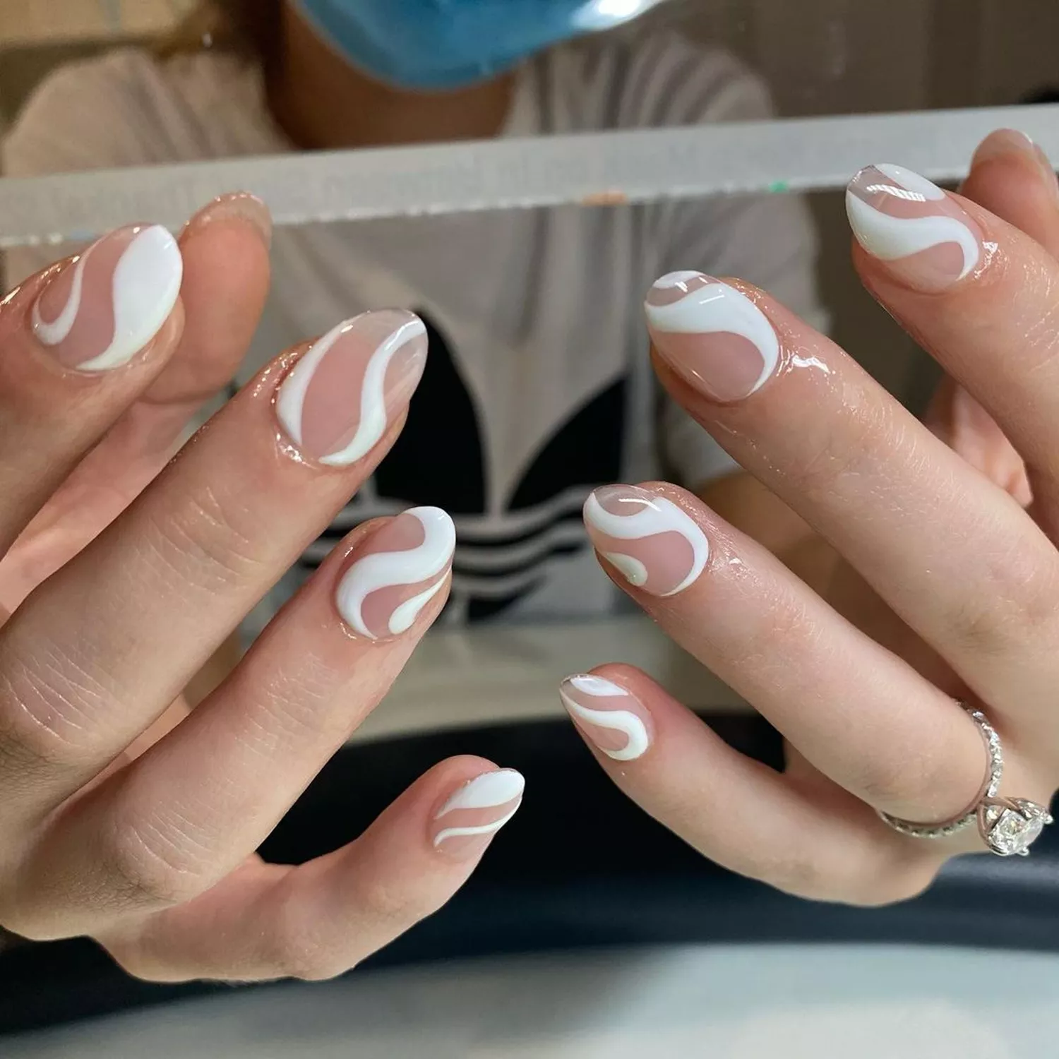 A person shows off their manicure, which features a light base and white swirl designs