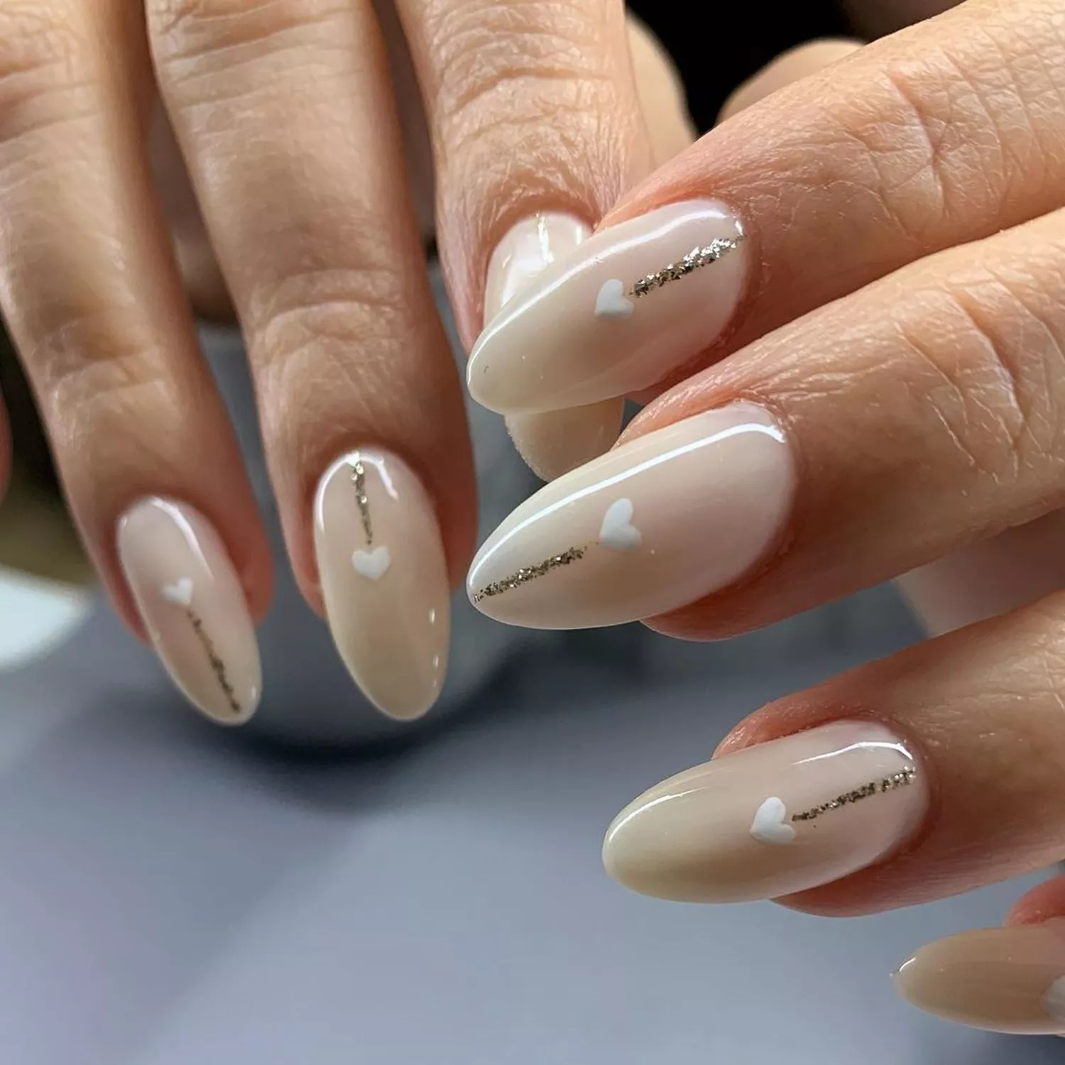 A person shows off their light nails that have gold line and white heart accents