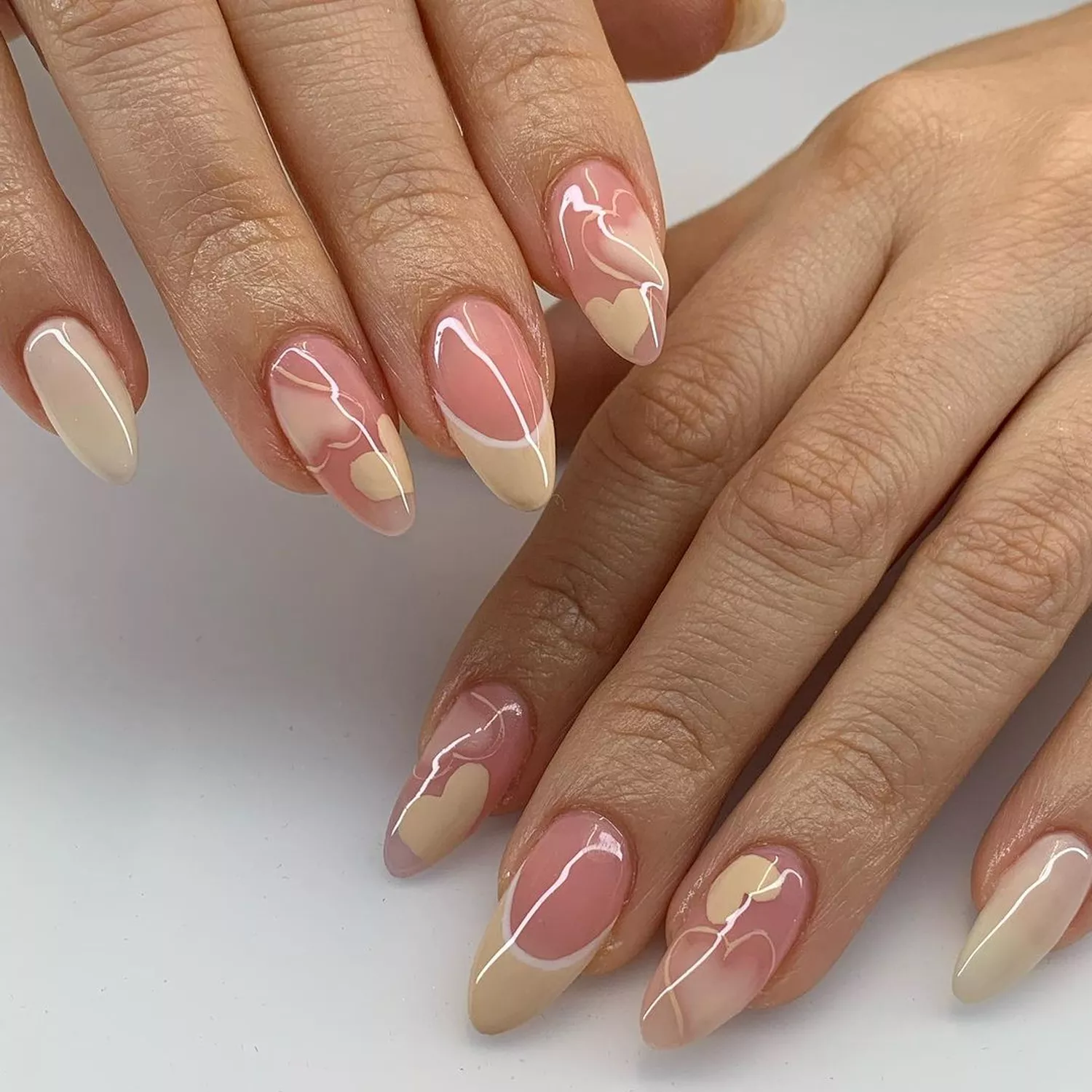 Glossy nude almond-shaped nails with heart accents and French tips