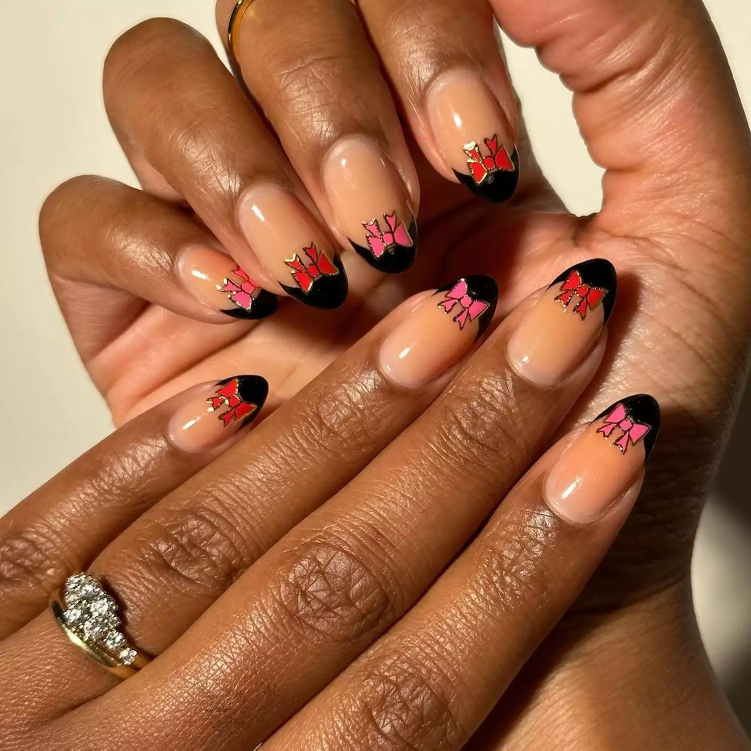 Black French manicure with pink and red bow accents on almond-shaped nails