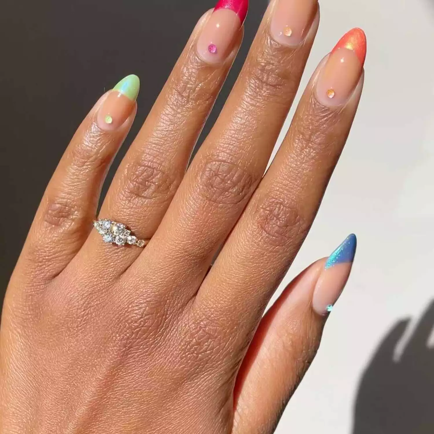 Almond-shaped nails with iridescent rainbow French tips and rhinestone cuticle accents