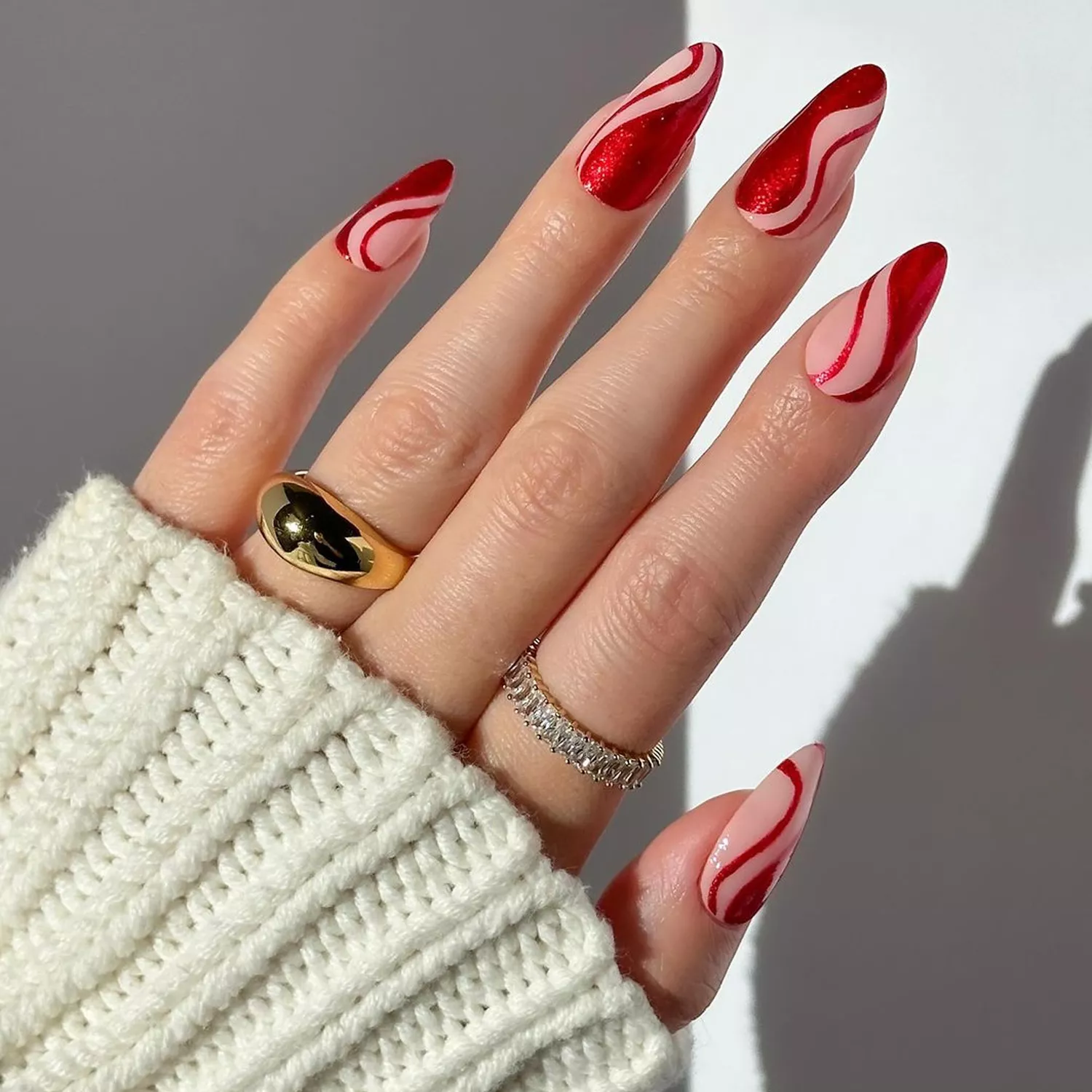 Hand showing red and white swirl nail art wearing a sweater and rings
