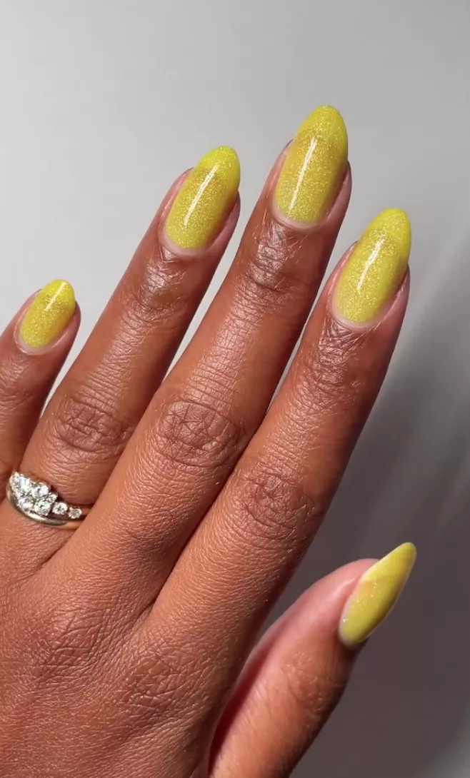 Person with almond-shaped nails painted in a glittery yellow-green polish