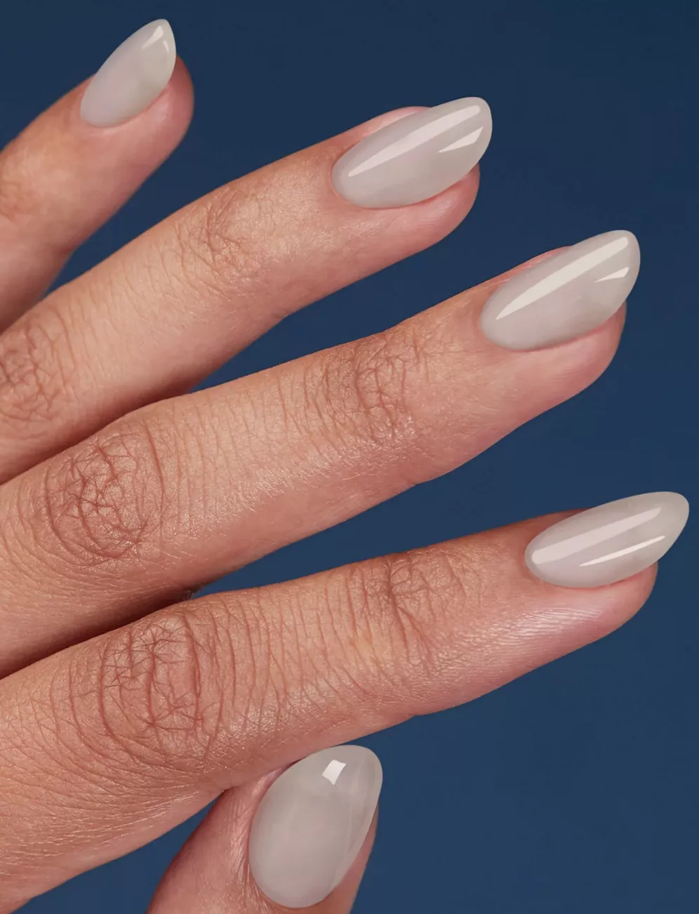 Person shows their oval-shaped nails painted in a sheer gray-white polish