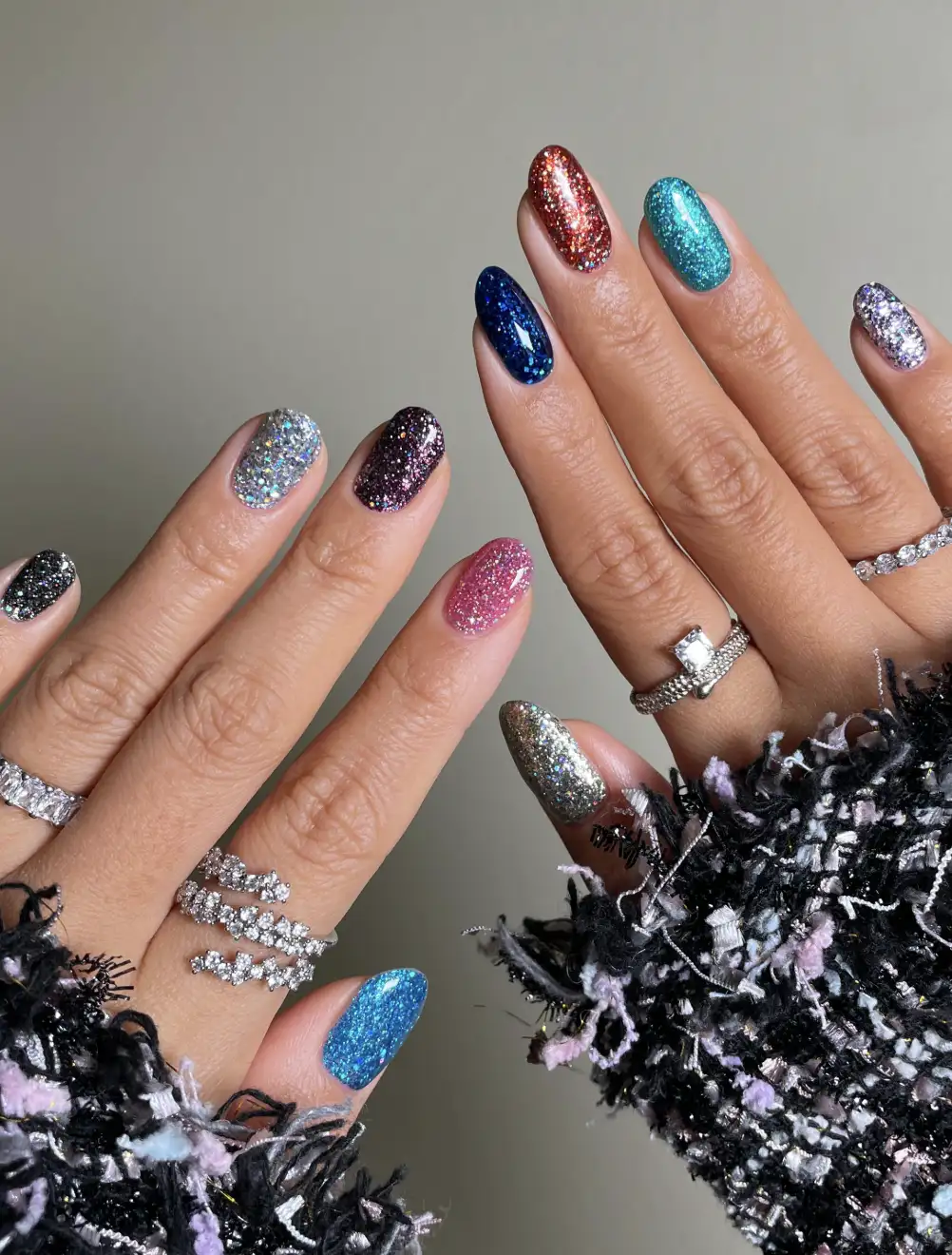 Manicured hands with multiple glitter nail polish colors and diamond rings