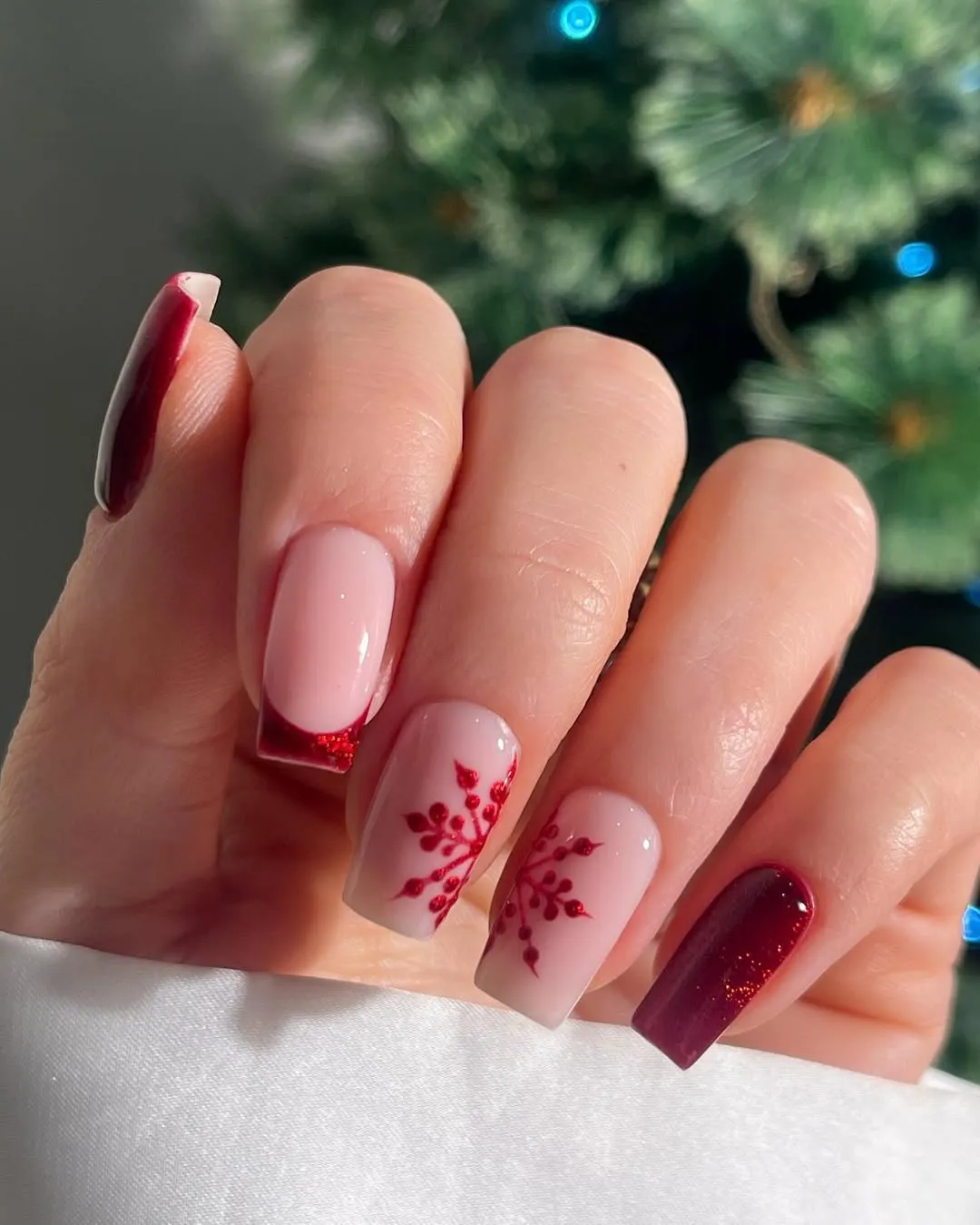 Square nails with sparkly red french tips and snowflake designs
