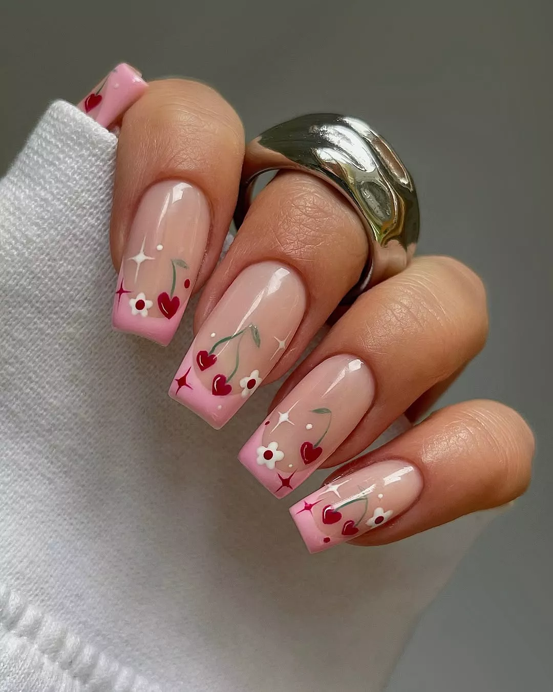 Person with long, square nails featuring pink French tips and hand-painted cherries and flowers