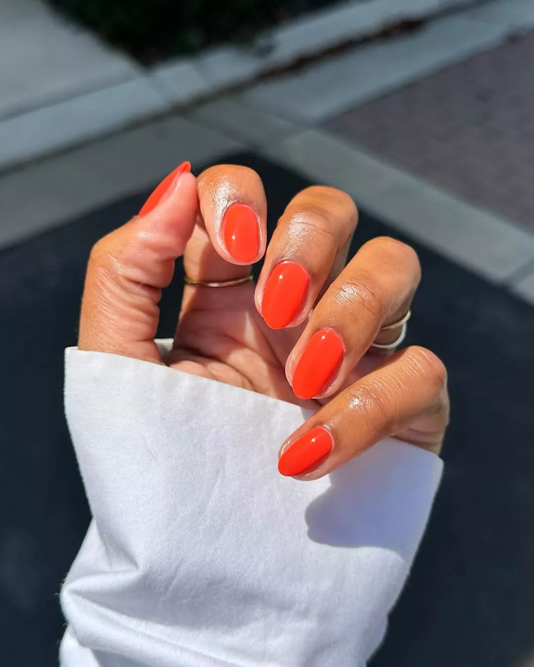 Person shows off their round nails, which are painted in a bright orange