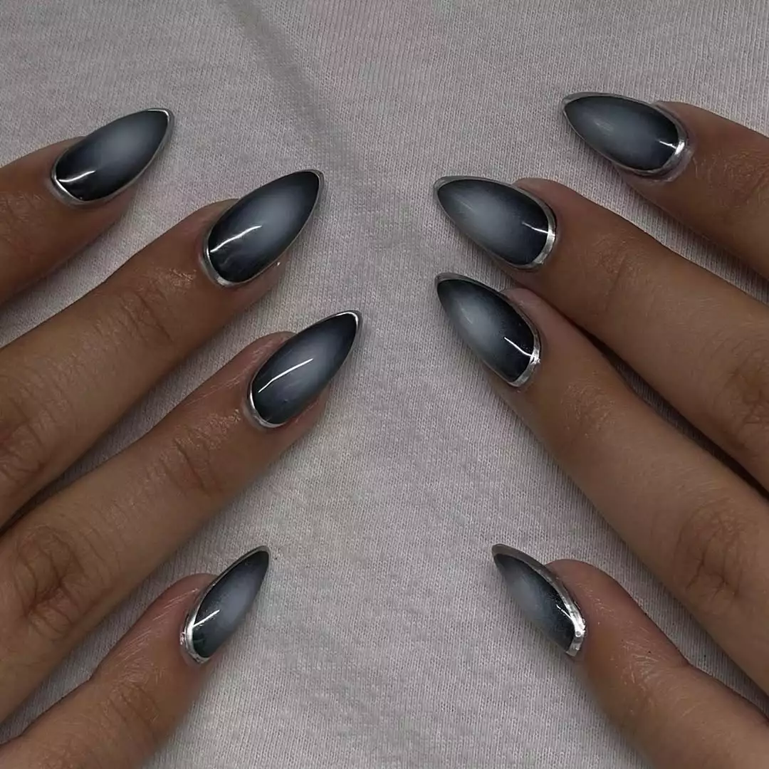 Hands with glossy stiletto-shaped nails that are outlined in metallic silver and aura in the middle