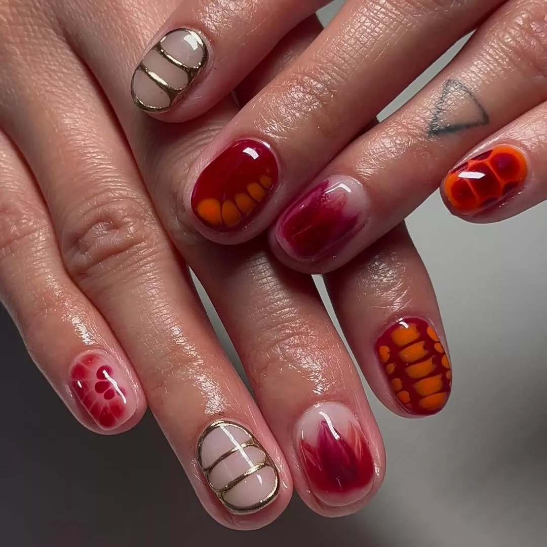 Person with short nails that have metallic and floral designs on each nail