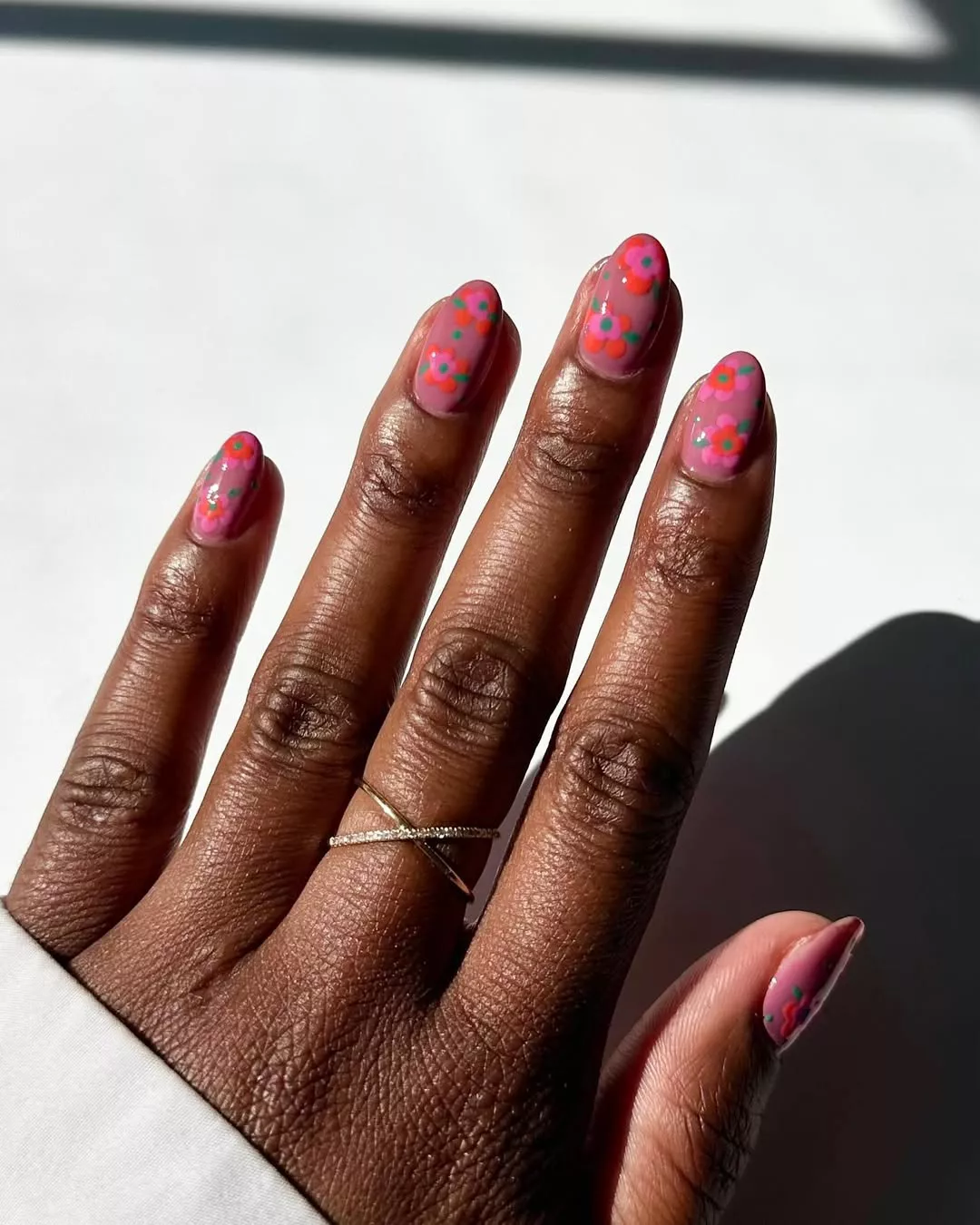 Person with round nails shows off their mauve manicure with hand-painted red and pink flowers