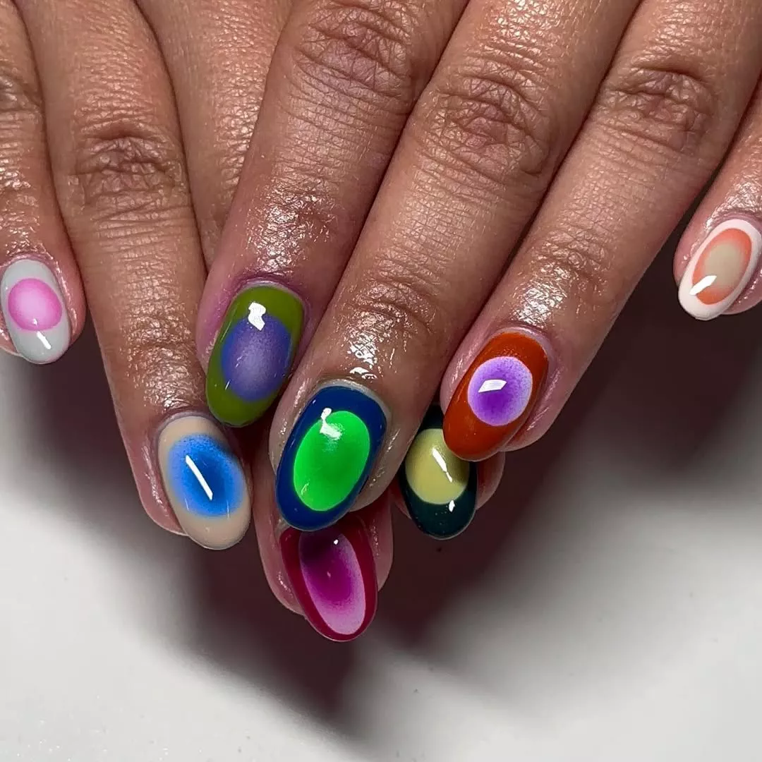 Person with short, round nails featuring circles in different colors on each nail