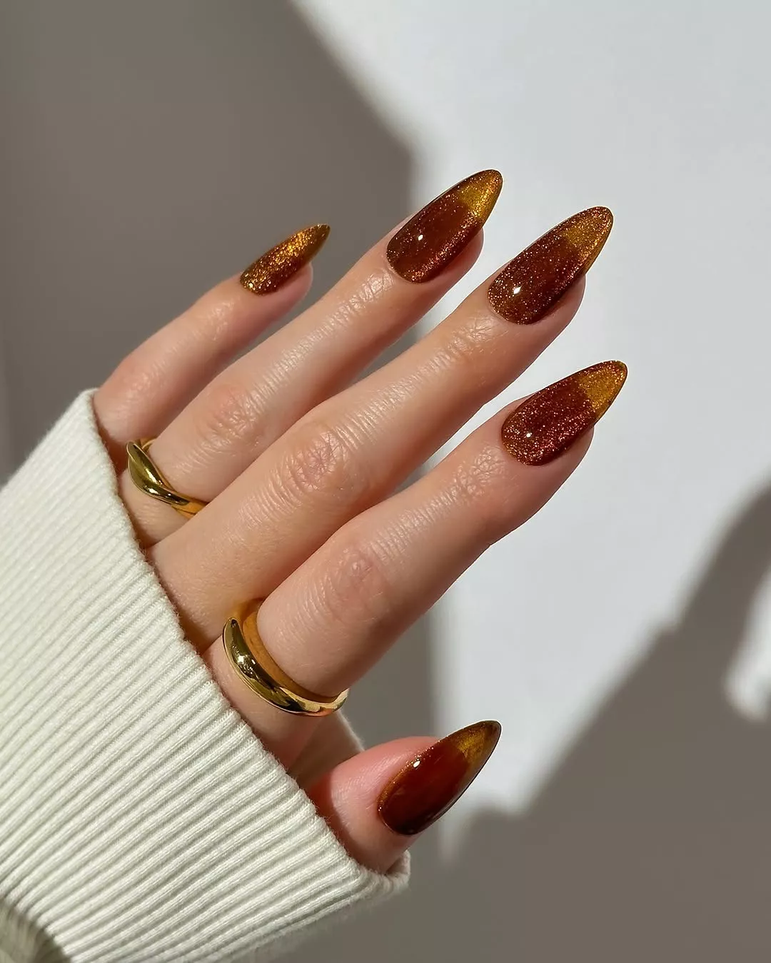 Person shows off their medium-length, almond-shaped jelly nails in a light brown with glitter