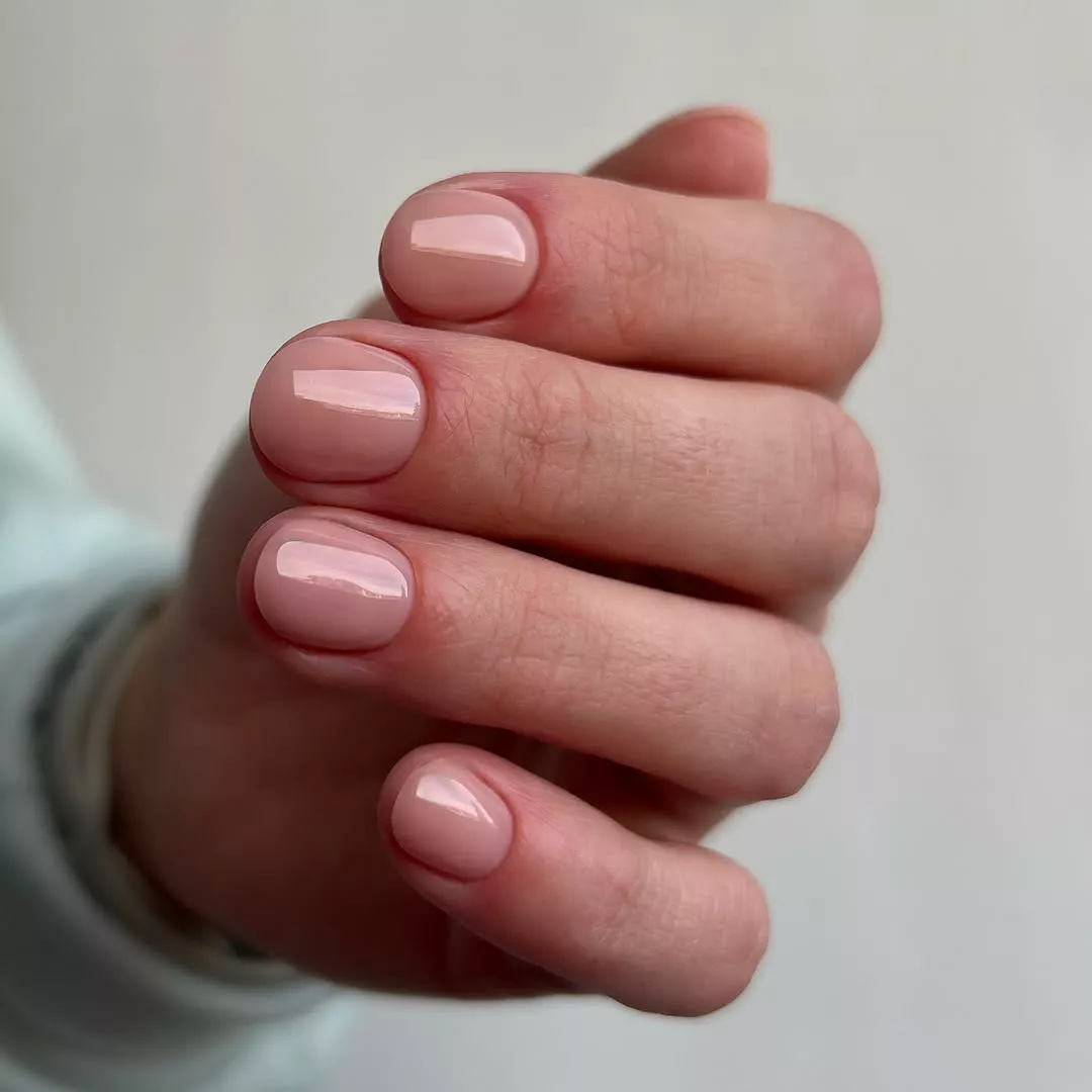 Person shows off their short, rounded nails, which are painted in a solid nude base
