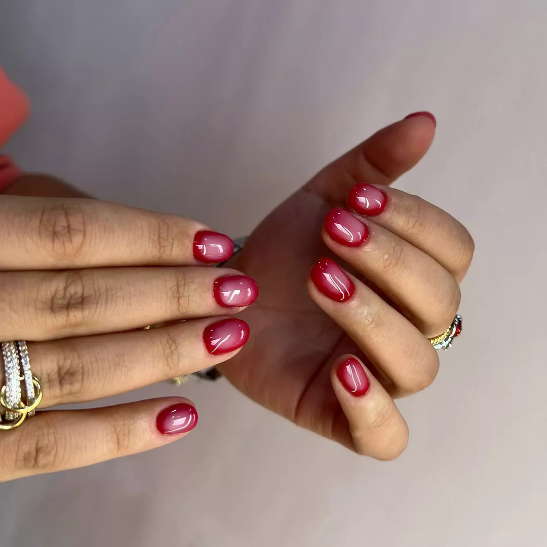 Person with rounded nails which are dark red on the edges and dusty pink in the middle