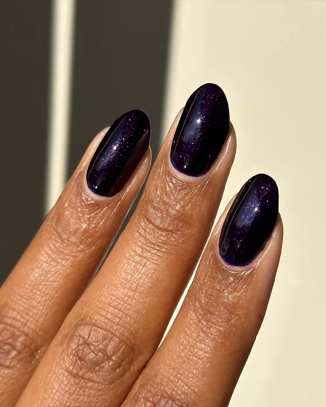 A person showing three fingers with nails painted in a glittery deep purple polish