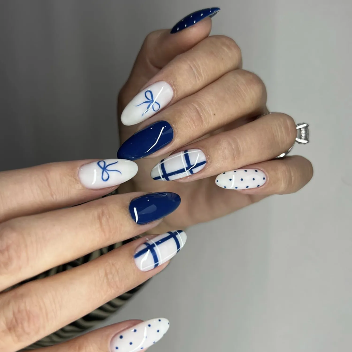 Hand with nail art featuring designs such as ribbons and dots on long polished nails