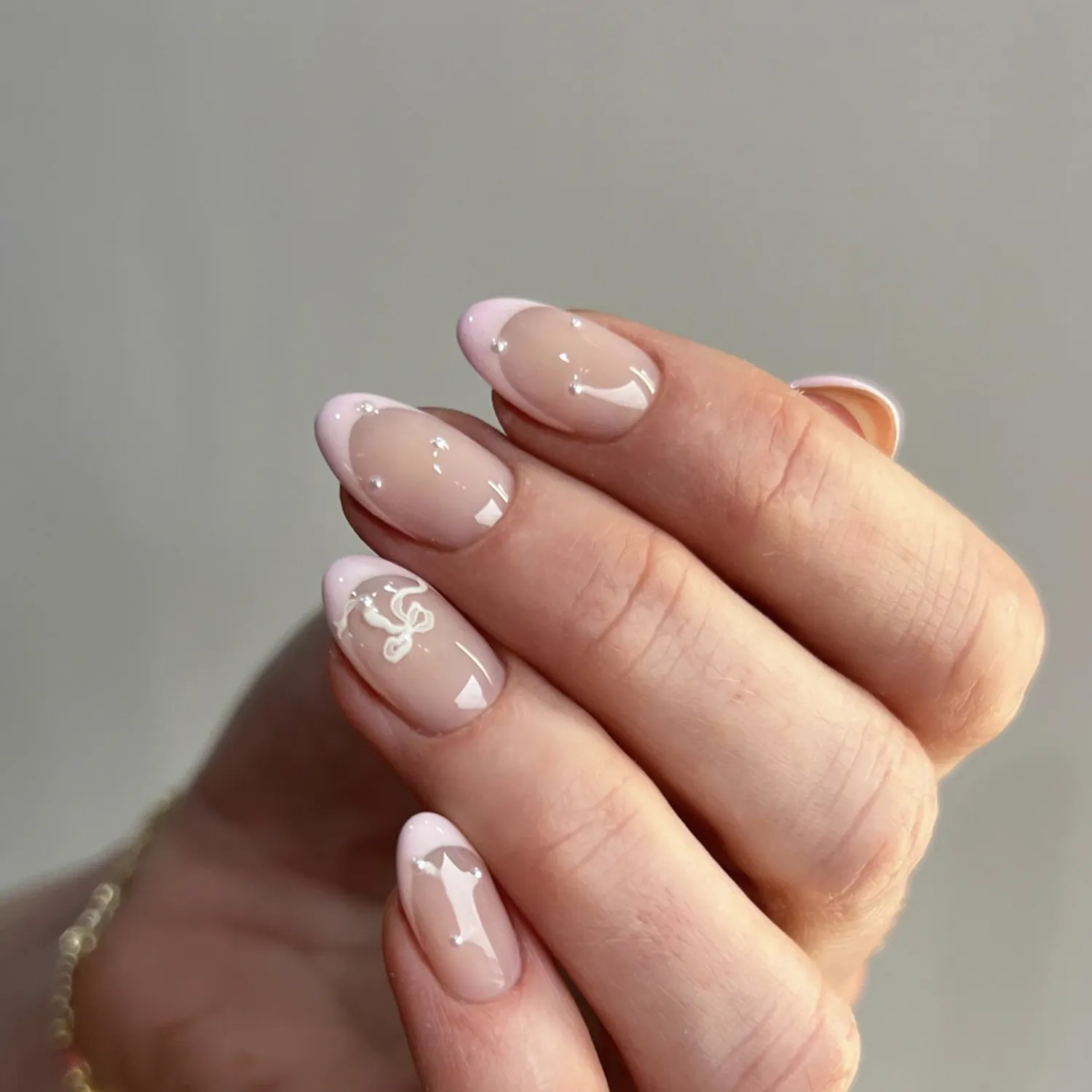 A closeup of a manicured hand with nail art featuring a bow and French tips