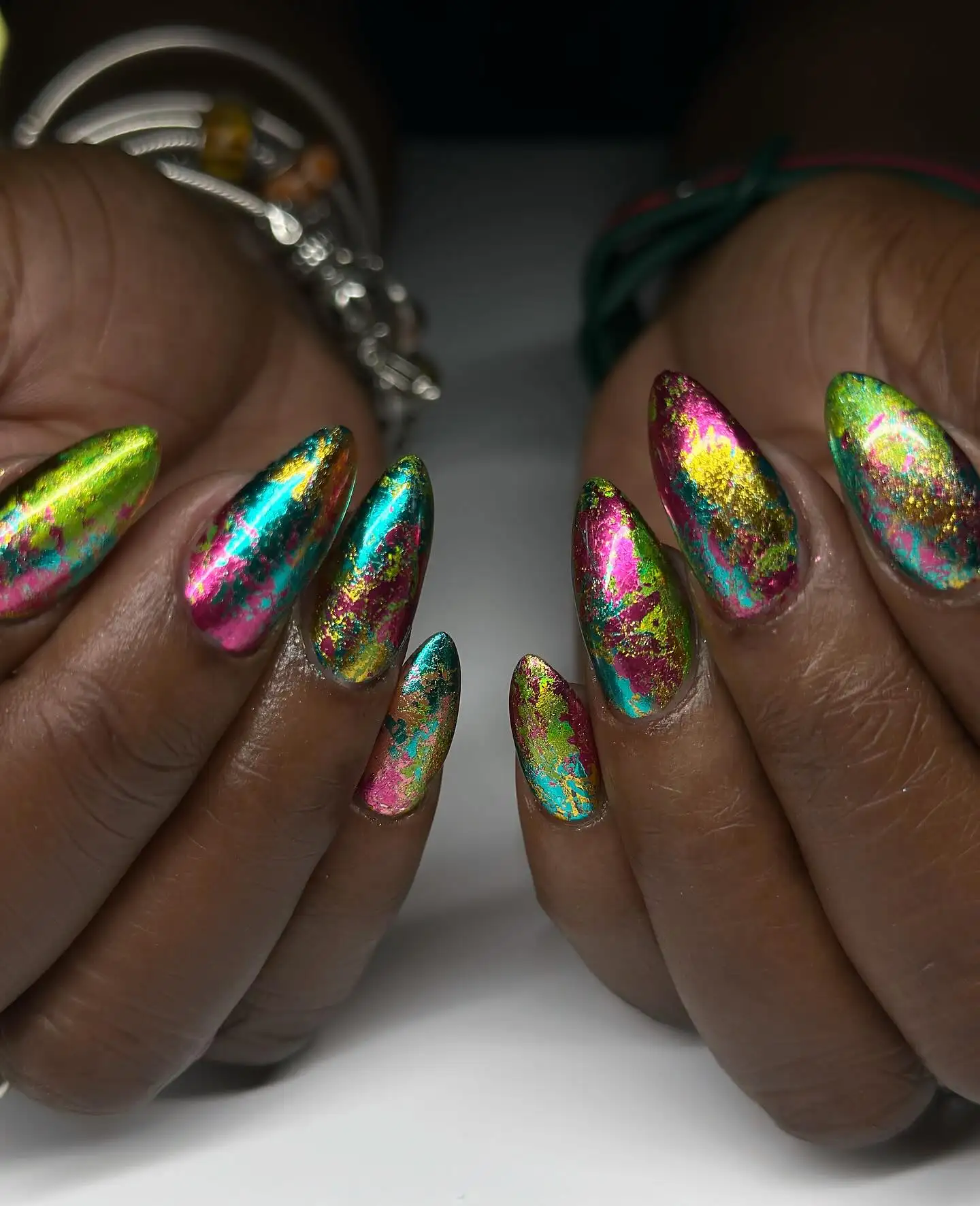 Colorful metallic nails featuring a blue, green, yellow, and pink foil pattern