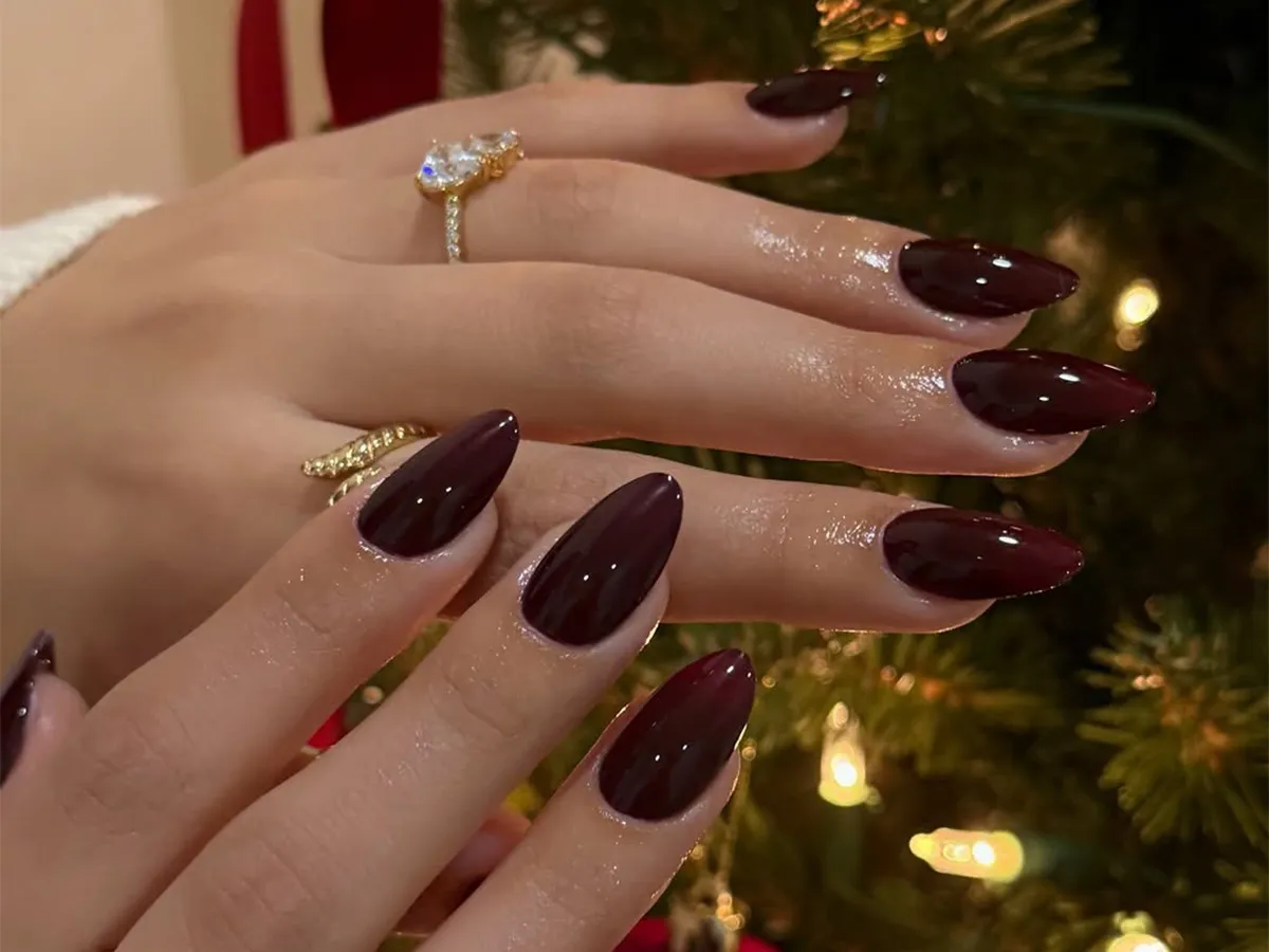 Closeup of hands with almondshaped painted nails jewelry and a holiday setting with a Christmas tree in the background