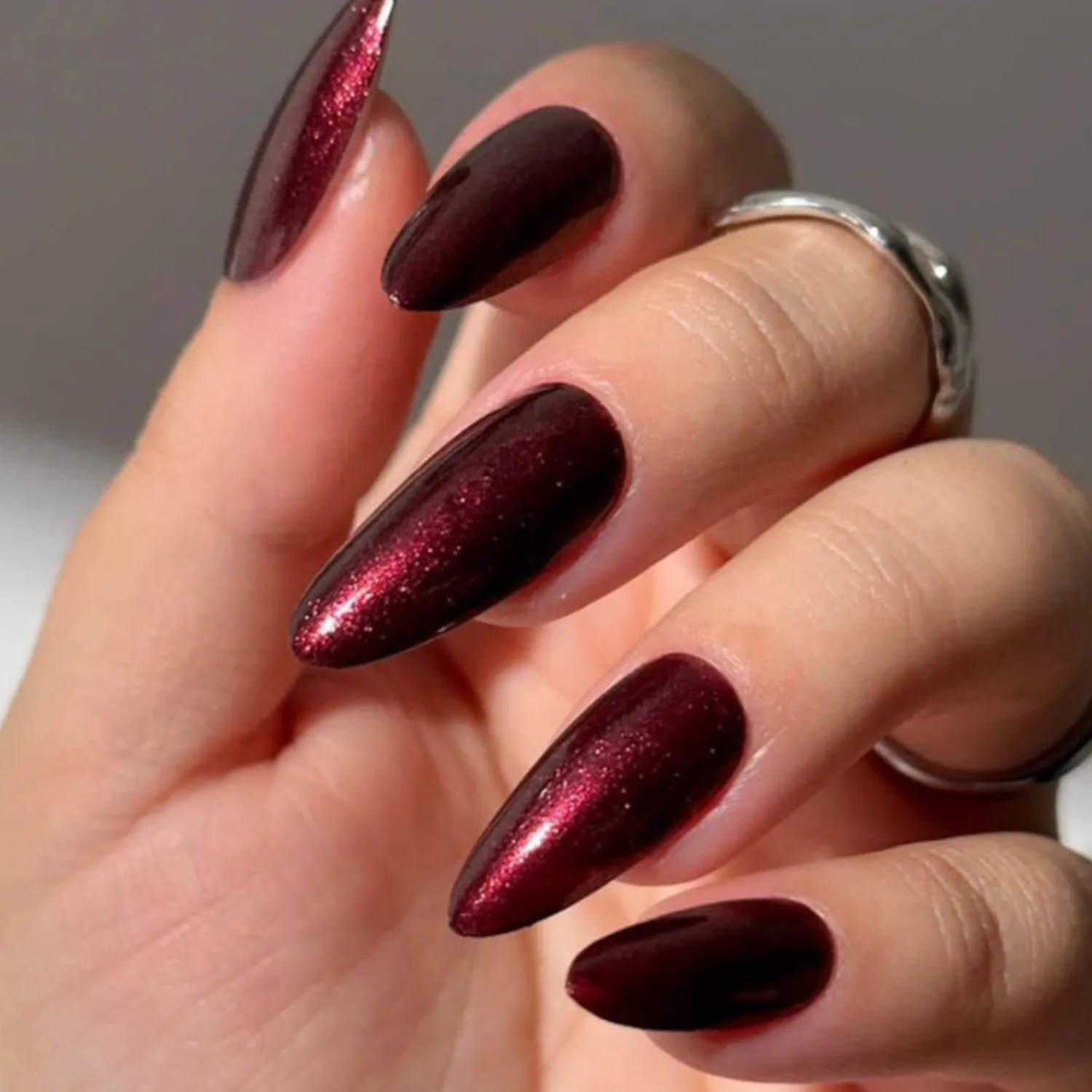 A persons hand with long dark metallicpainted nails and a ring on one finger