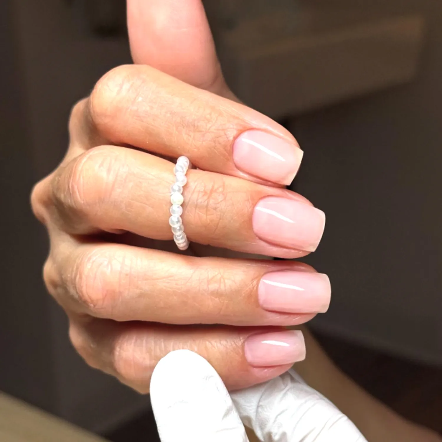 Closeup of a manicured hand wearing a ring with a gloved hand supporting it