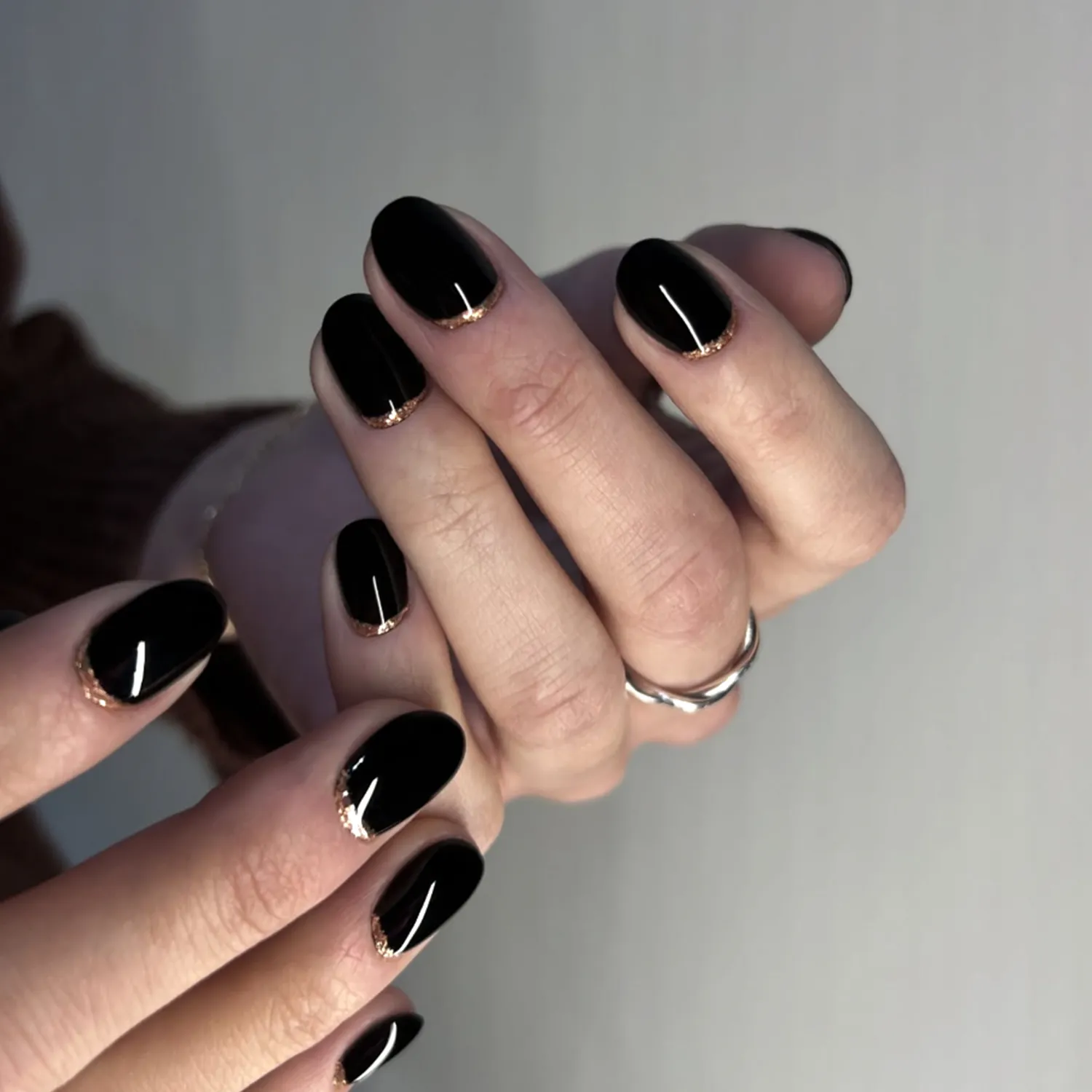 Hands with glossy blackpainted nails featuring subtle gold details