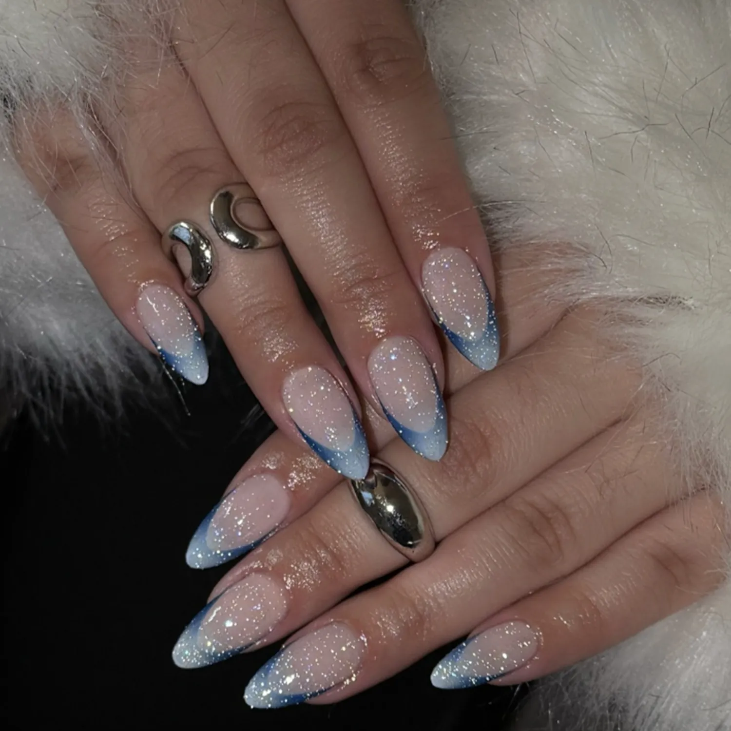 Hands featuring bluetipped nails with glitter accents adorned with silver rings