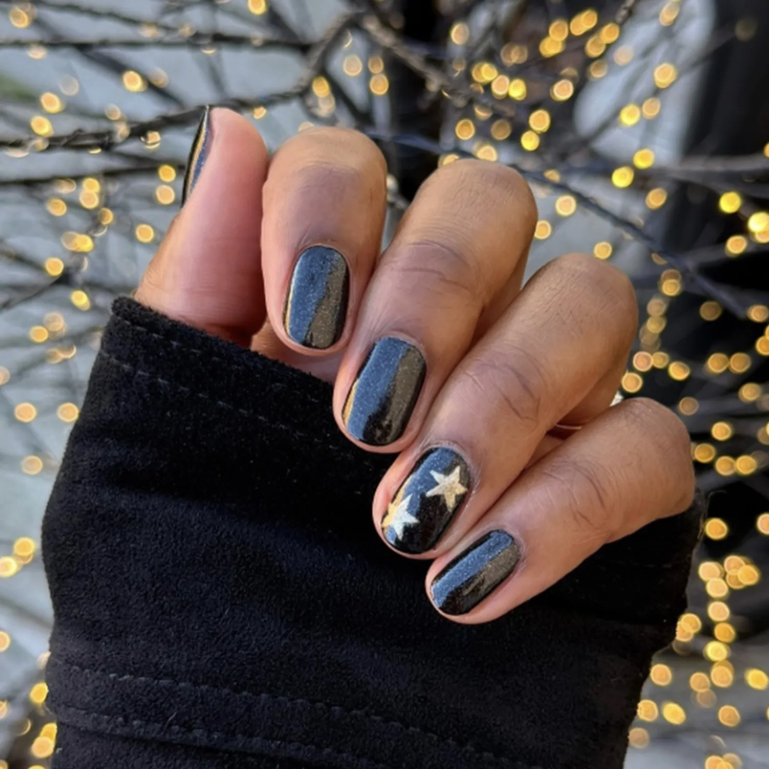 A hand with festive darkcolored nail polish and gold star accents festive holiday design