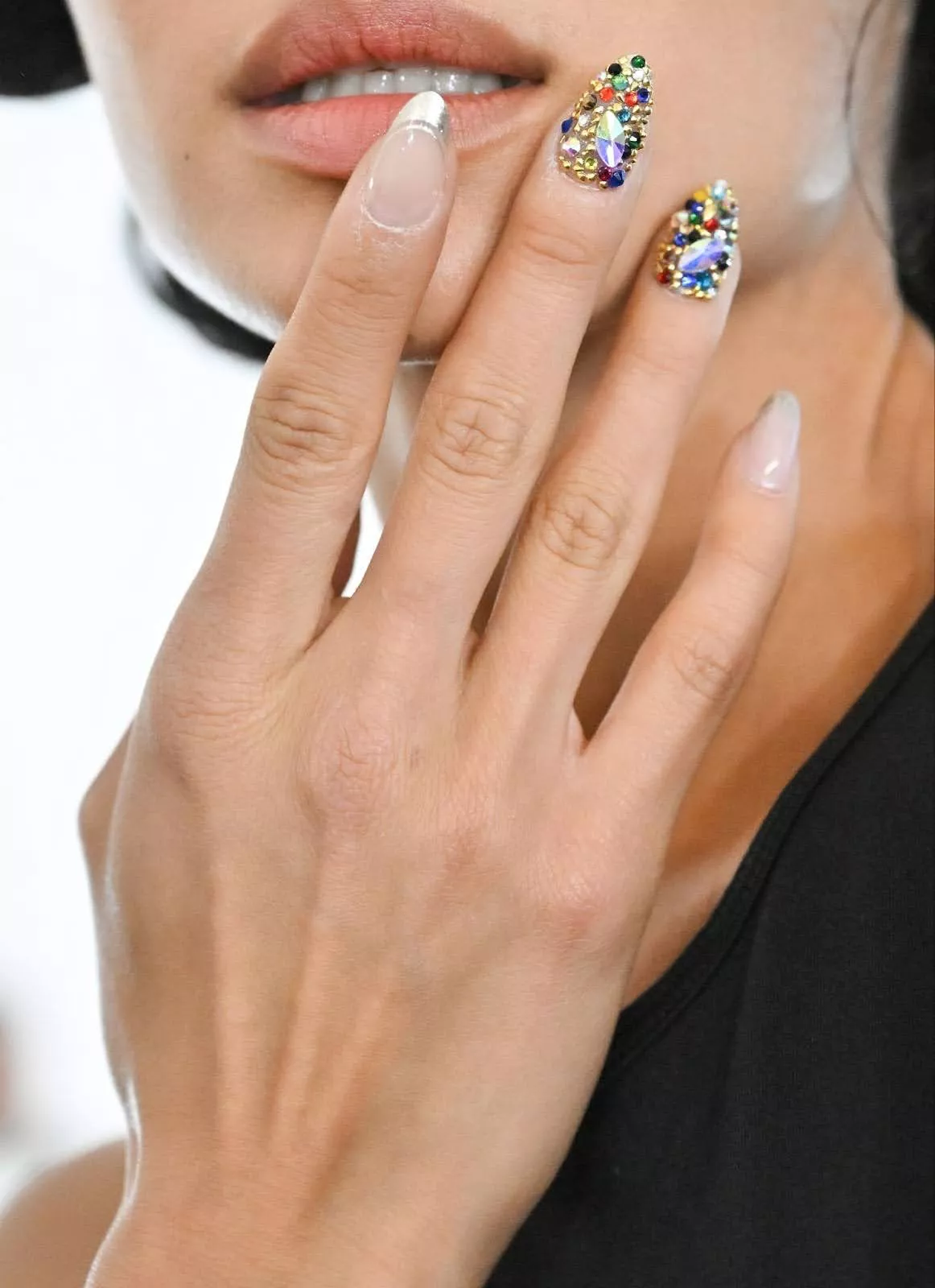 Person shows off their colorful gem nails, which are in an almond shape