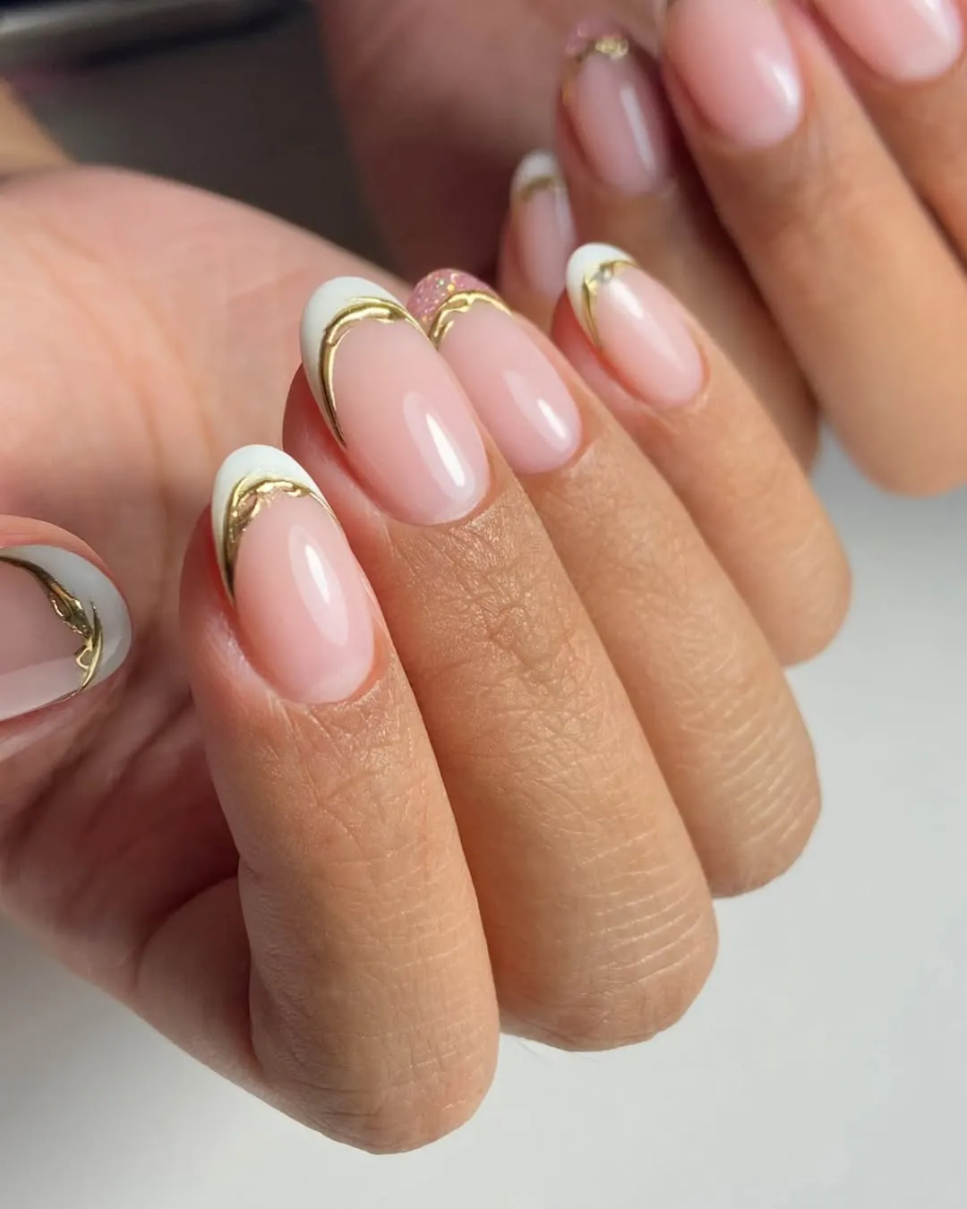 A person showing off a French manicure with gold details