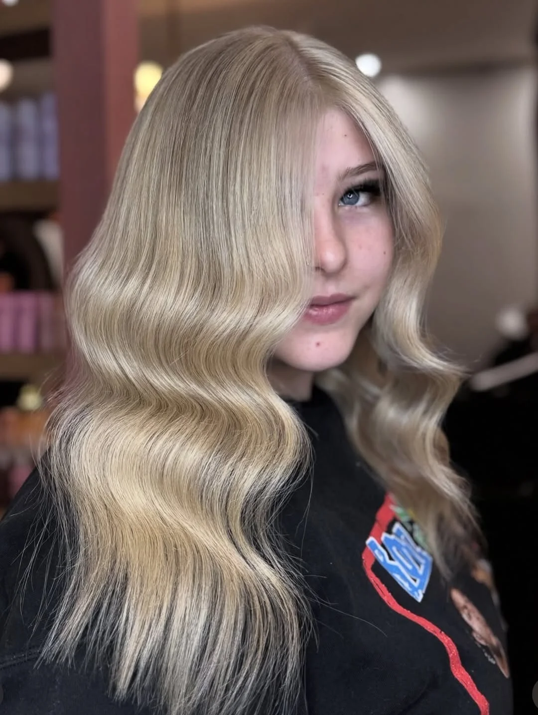 A woman with long blonde hair styled in a chic, voluminous bun, perfect for long hair summer hairstyles 2026. She wears a cream-colored off-the-shoulder top for a sophisticated look.