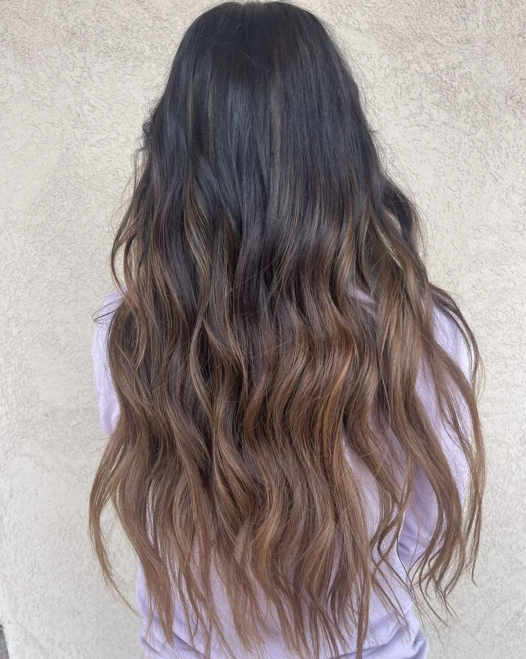 Close-up of a woman with long, sun-kissed hair styled in a messy, braided ponytail, perfect for long hair summer hairstyles 2026. She's wearing a casual white off-the-shoulder top.