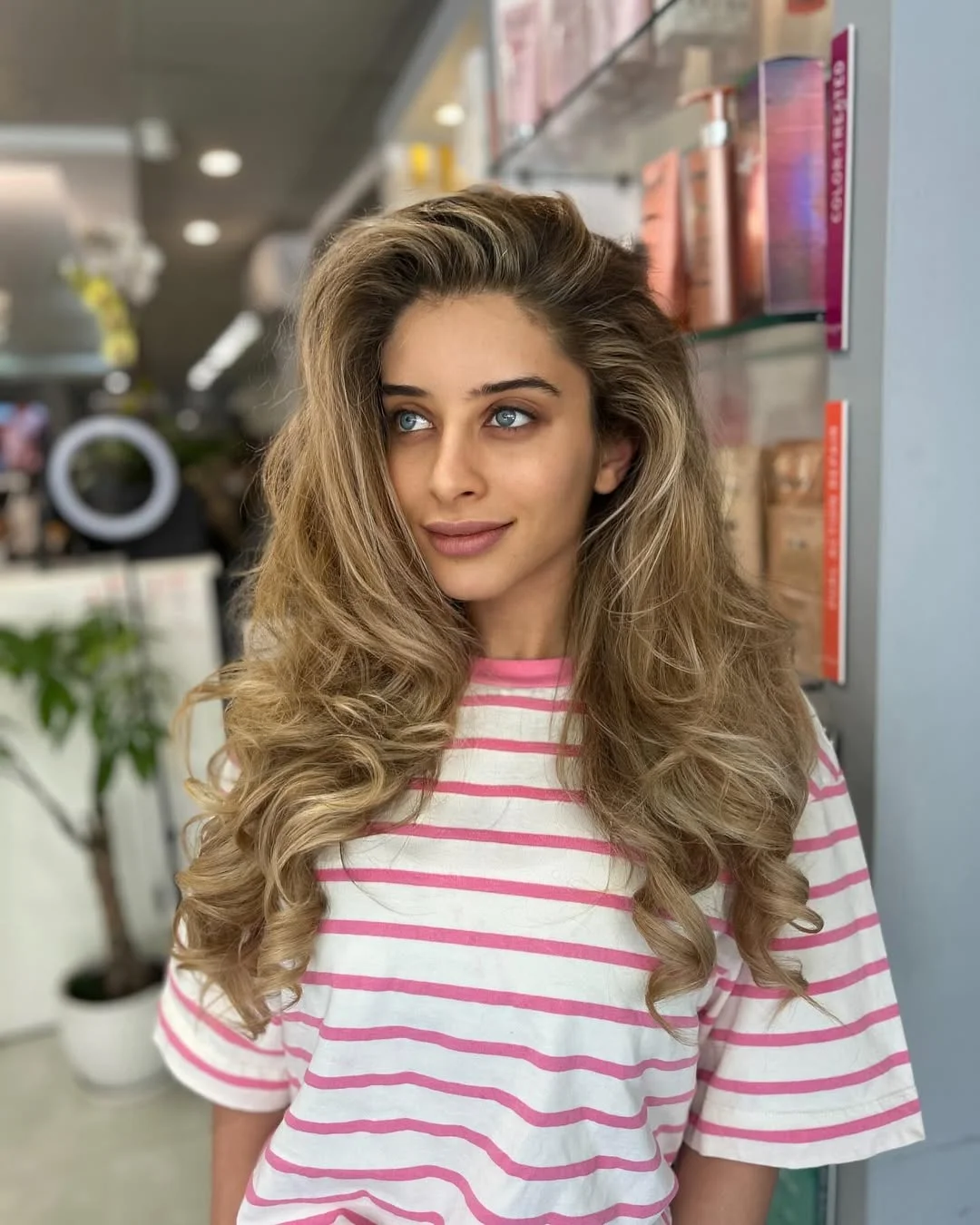 Woman with long, wavy blonde hair styled in a chic ponytail, perfect for long hair summer hairstyles 2026. She wears a flowy white sundress, ideal for a beach or casual outdoor event.
