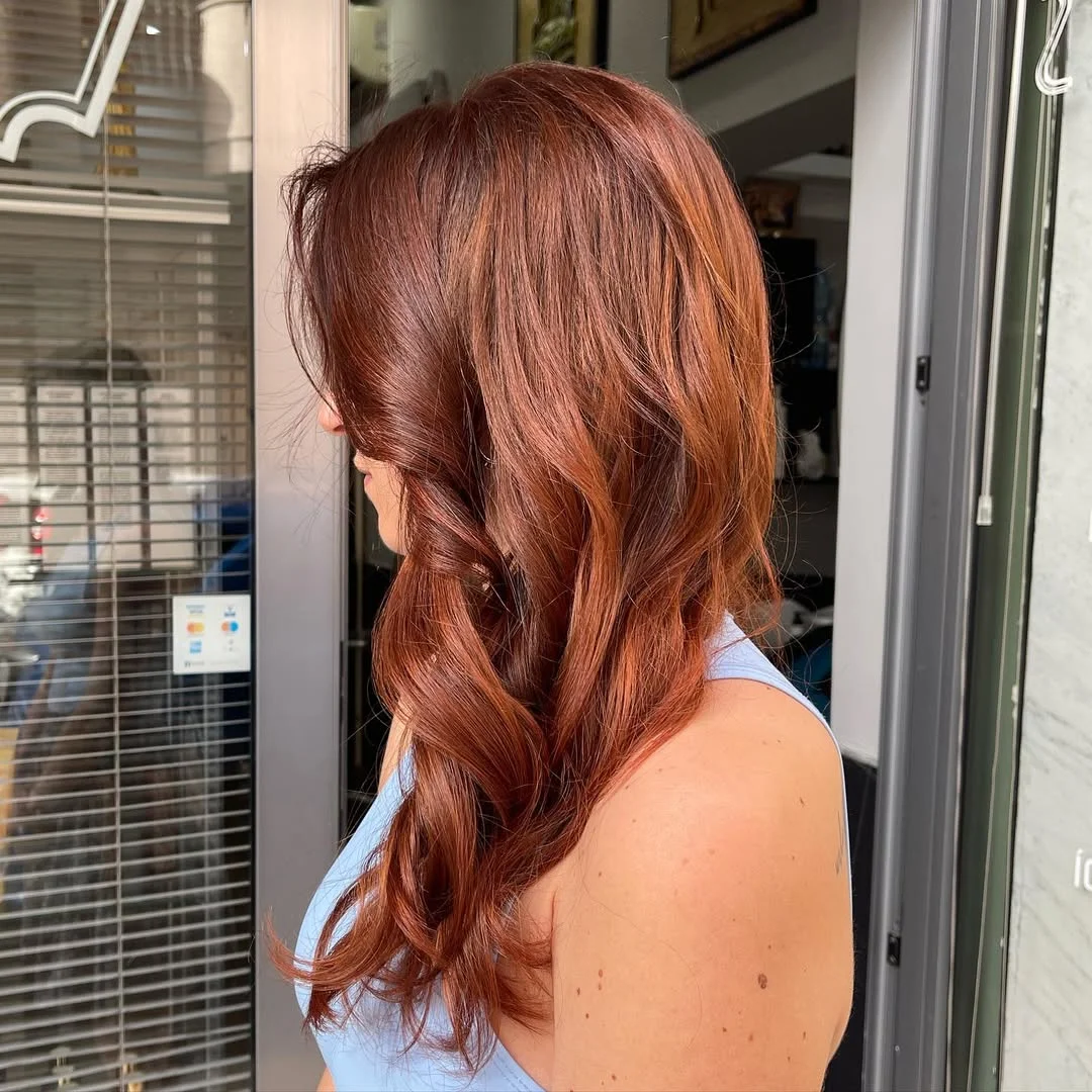 Woman with vibrant copper hair smiling outdoors, showcasing a perfect look for copper hair summer ideas 2026. Her hairstyle complements her complexion.